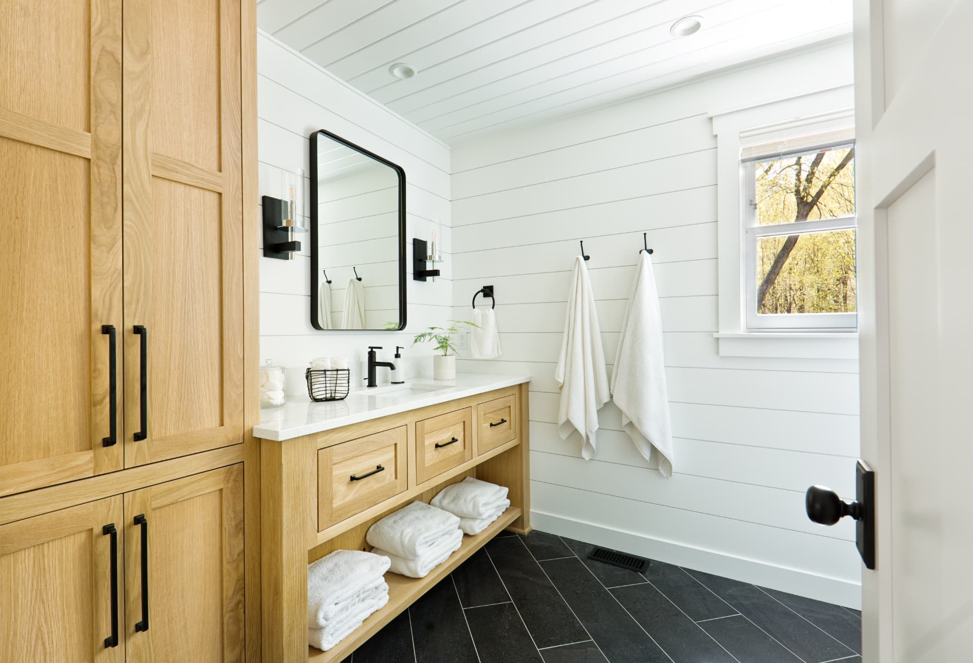 Bright modern bathroom with white shiplap walls, oak vanity, and black fixtures