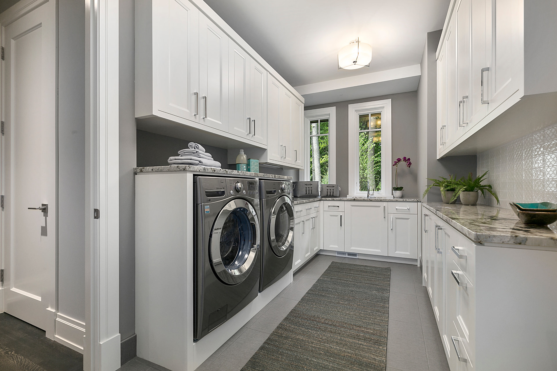 Bright custom laundry room with white shaker cabinets, granite countertops, and stainless appliances